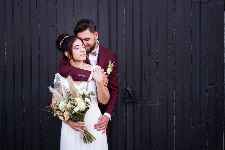 photo d'un couple de jeunes mariés qui s'enlace, le marié a un costume bordeaux